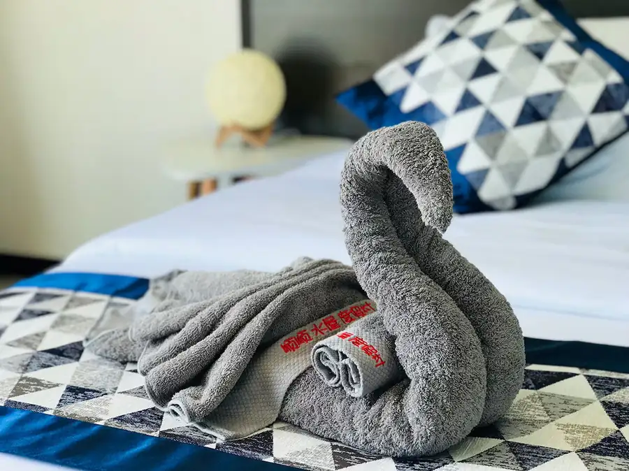 A close-up view of an intricately folded grey towel swan on a bed at WB Shun Shun Water Bungalows